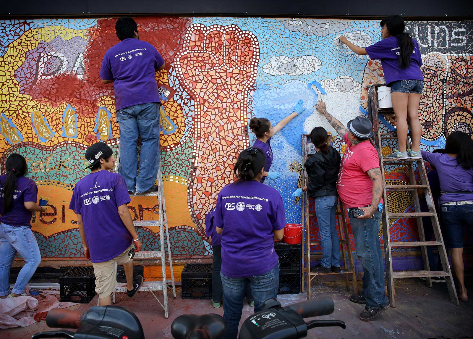 people in purple shirts painting a public mural